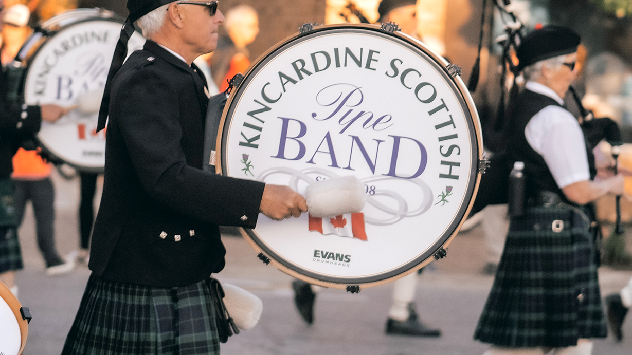 A drummer marches and plays a bass drum that reads "Kincardine Scottish Pipe Band."