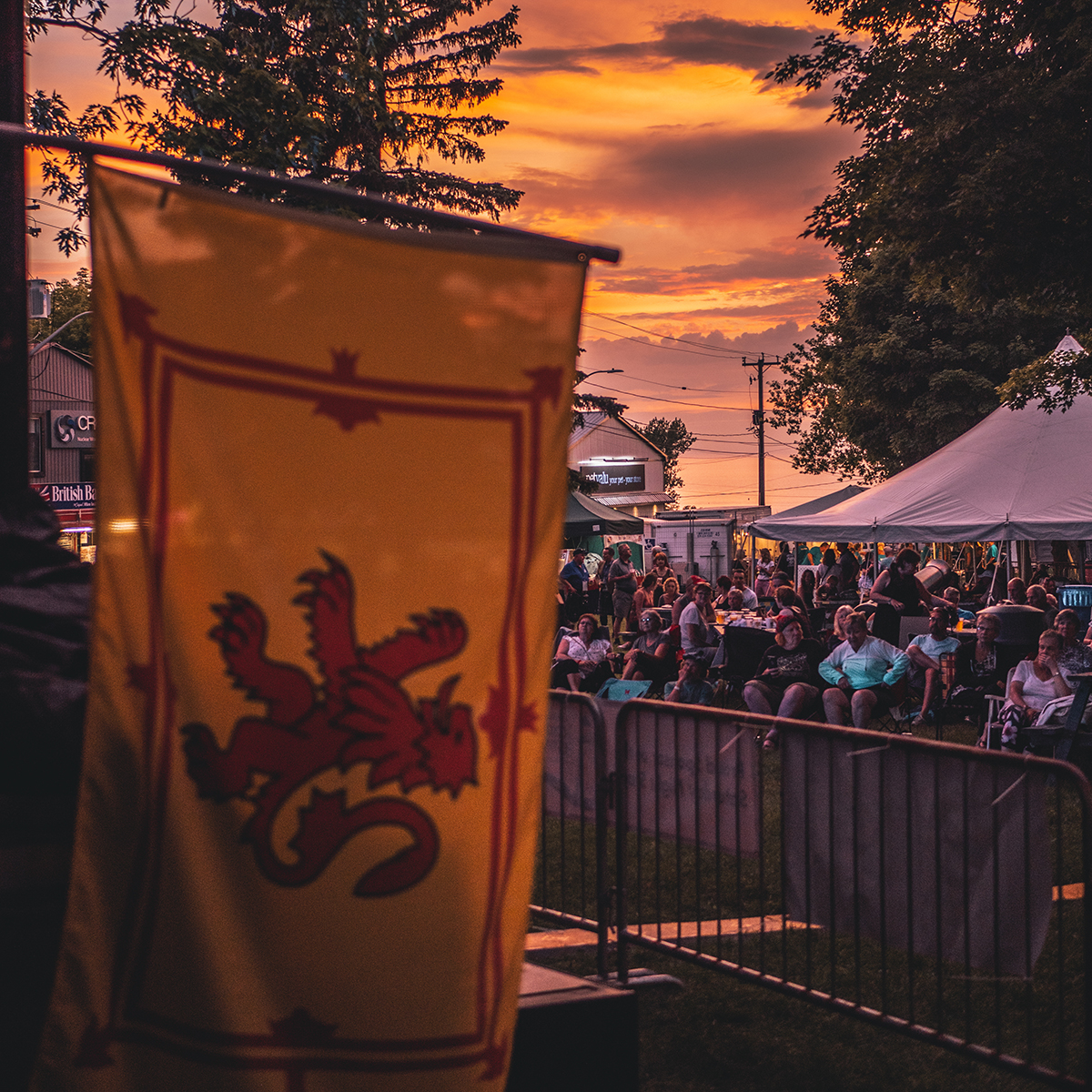 A Scottish flag hangs in front of a large crowd gathered at sunset for the Scottish Festival and Highland Games.